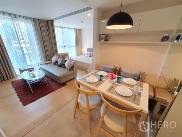 Condominium for rent in Watthana, Bangkok - Living and dining area featuring a grey sofa, round coffee table and four-seat dining set under a pendant light.