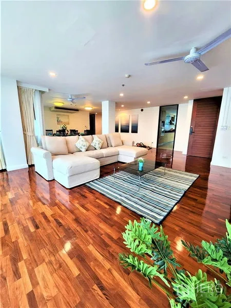 Condominium for rent in Bang Rak, Bangkok - Living room with L-shaped sofa, ceiling fans, and glossy hardwood floors.