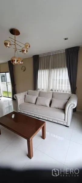 Detached House for rent in Lat Krabang, Bangkok - Bright living room with plush sofa, coffee table and large curtained windows