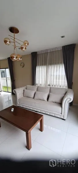 Detached House for rent in Lat Krabang, Bangkok - Bright living room with plush sofa, coffee table and large curtained windows