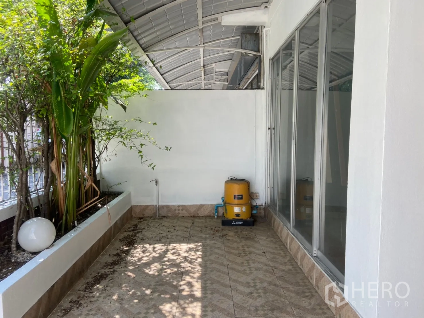 Townhouse for rent in Watthana, Bangkok - Shaded front terrace with planter, sliding glass doors and a utility water pump.