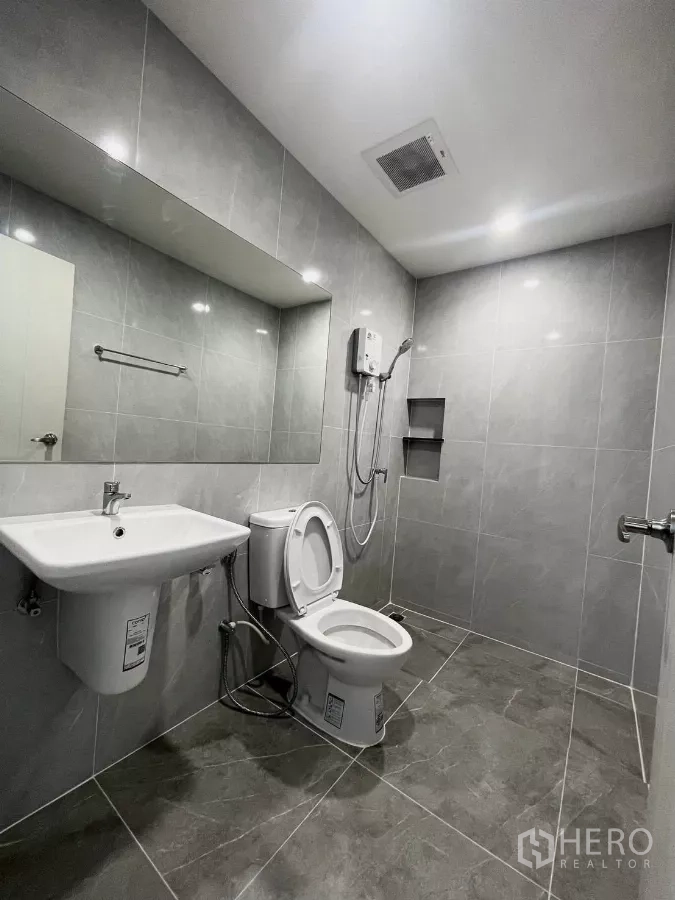 Townhouse for rent in Samut Prakan - Bathroom finished in grey tiles with wide mirror, shower and toilet.