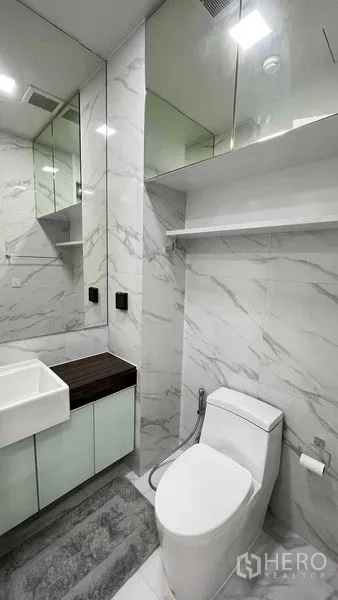 Condominium for rent in Watthana, Bangkok - Modern bathroom with white marble tiles, vanity, mirrored cabinets and toilet.