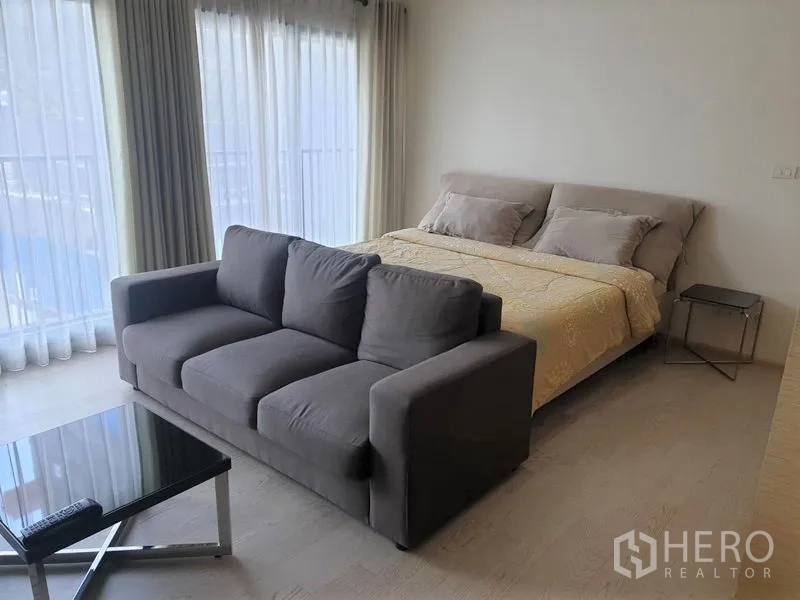 公寓 出租在Khlong Toei, Bangkok - 明亮的睡眠区，配大床、灰色沙发与转角落地窗