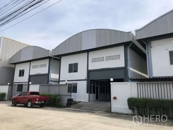 Warehouse for rent in Pak Kret, Nonthaburi - Modern warehouse block in Pak Kret with arched metal roof, gated frontage and wide roller shutter doors.