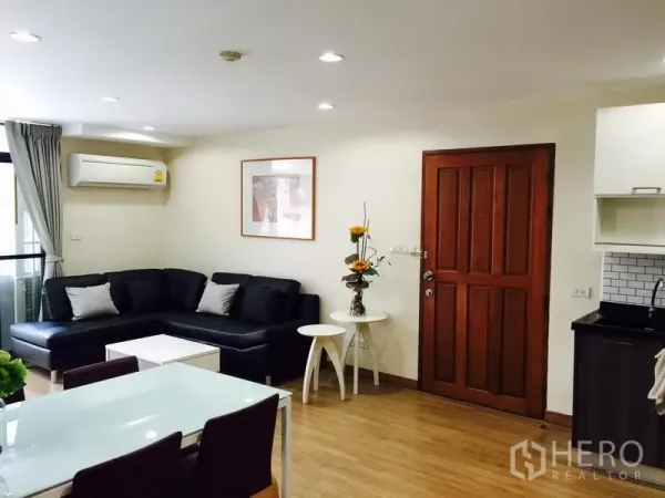 公寓 出租在Watthana, Bangkok - 明亮的客餐厅，黑色转角沙发、木地板与空调