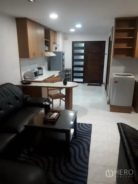 公寓 出租在Watthana, Bangkok - 开放式客厅，黑色皮沙发、茶几与厨房一体并带洗衣机。