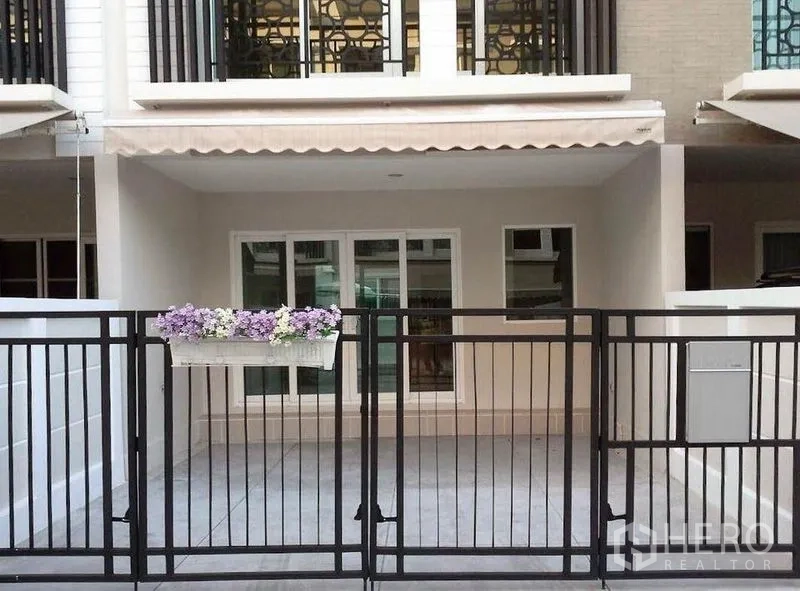 Townhouse for sale in Bang Kapi, Bangkok - Townhouse frontage with gated covered carport, sliding glass entrance, and awning.