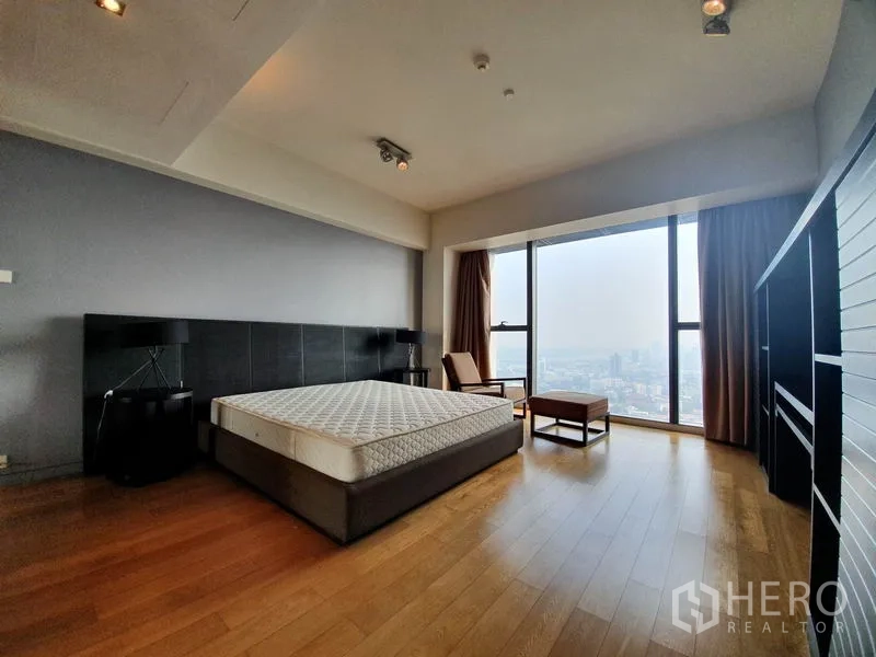 Condominium for rent in Sathon, Bangkok - Expansive master bedroom with wood floors, lounge chair and wide city-view windows.