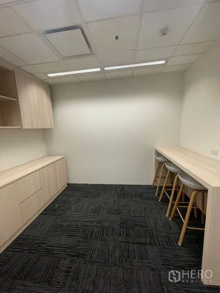Office Space for rent in Dusit, Bangkok - Pantry area with light wood built-in cabinets, bar counter and stools under ceiling lights.