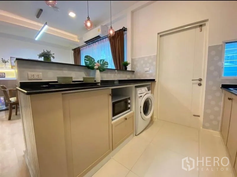 Townhouse for rent in Prawet, Bangkok - Kitchen peninsula with black countertop, built-in microwave and washer under pendant lights.