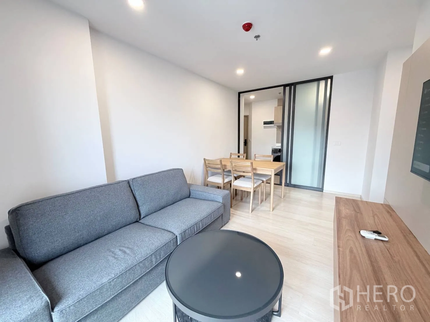 公寓 for rent in Din Daeng, Bangkok - 开放式起居空间，灰色沙发与茶几旁是餐桌，靠近厨房入口。