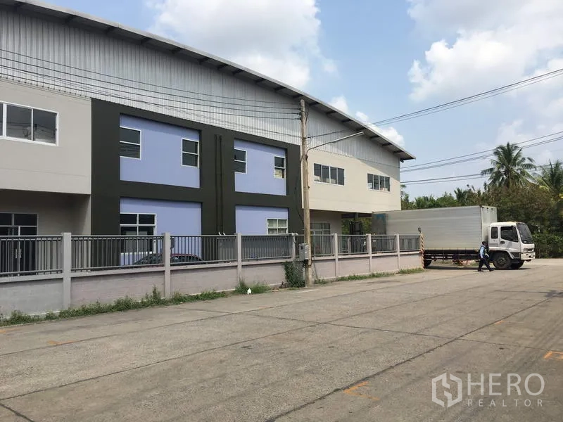 Factory for rent in Pathum Thani - Wide yard in front of modern factory units with truck loading area and perimeter fence.