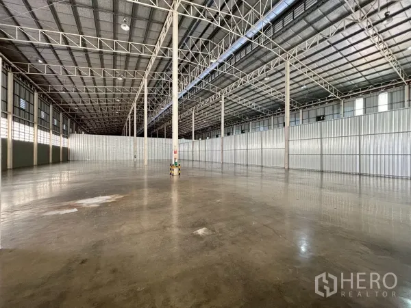 Warehouse for rent in Bang Sue, Bangkok - Empty storage hall with polished concrete slab, louvered windows and fire safety signage on columns.