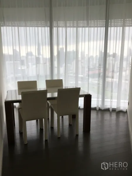 公寓 出租在Pathum Wan, Bangkok - 餐区设四把白色餐椅与玻璃餐桌，落地纱帘旁享城市景观。