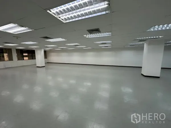 办公空间 出租在Watthana, Bangkok - 大型空置办公楼层，格栅天花灯、白墙、灰色乙烯基地面与结构柱。