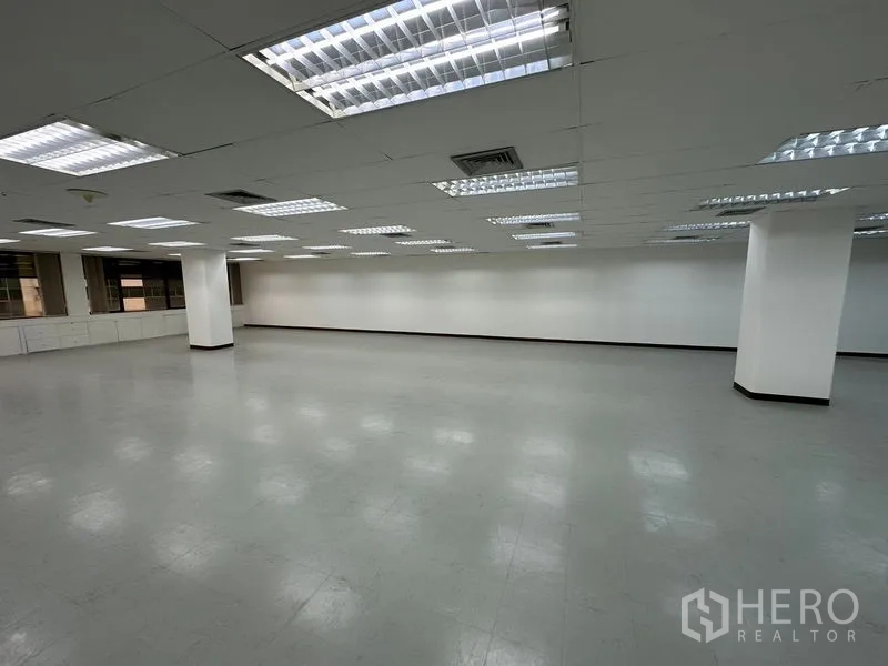 办公空间 出租在Watthana, Bangkok - 大型空置办公楼层，格栅天花灯、白墙、灰色乙烯基地面与结构柱。
