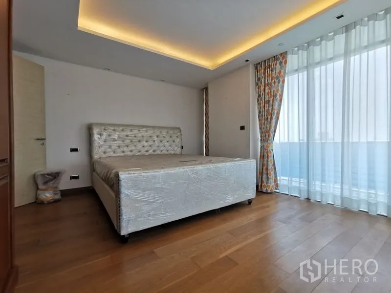 Condominium for rent or sale in Phaya Thai, Bangkok - Guest bedroom with tufted bed, recessed lighting, and floor-to-ceiling windows with curtains.