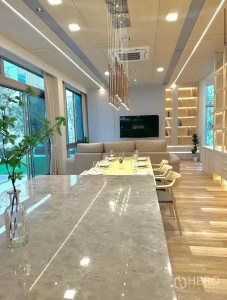 Detached House for rent in Saphan Sung, Bangkok - Open‑plan kitchen and dining with long stone island, pendant lighting and sofa seating beside floor‑to‑ceiling windows.