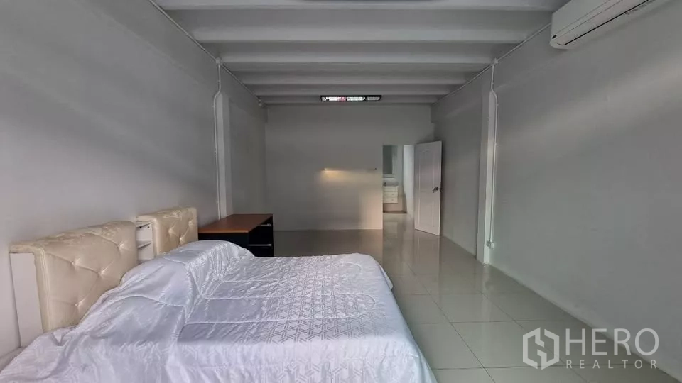Townhouse for rent in Huai Khwang, Bangkok - Spacious bedroom with bed, desk, tiled floor and air conditioning.