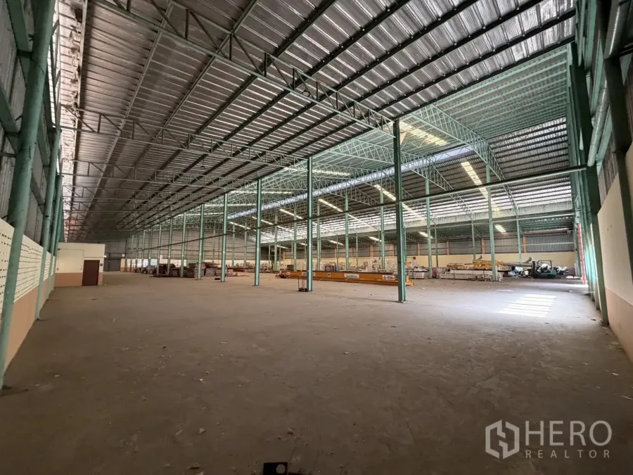 Factory for rent in Bang Na, Bangkok - Vast factory interior with high metal roof, green steel columns, and a concrete floor.