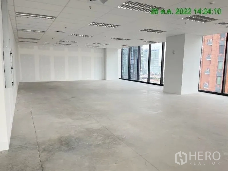 办公空间 出租在Ratchathewi, Bangkok - 宽敞未精装的办公楼层，转角大面积玻璃、白色隔墙与网格灯光。