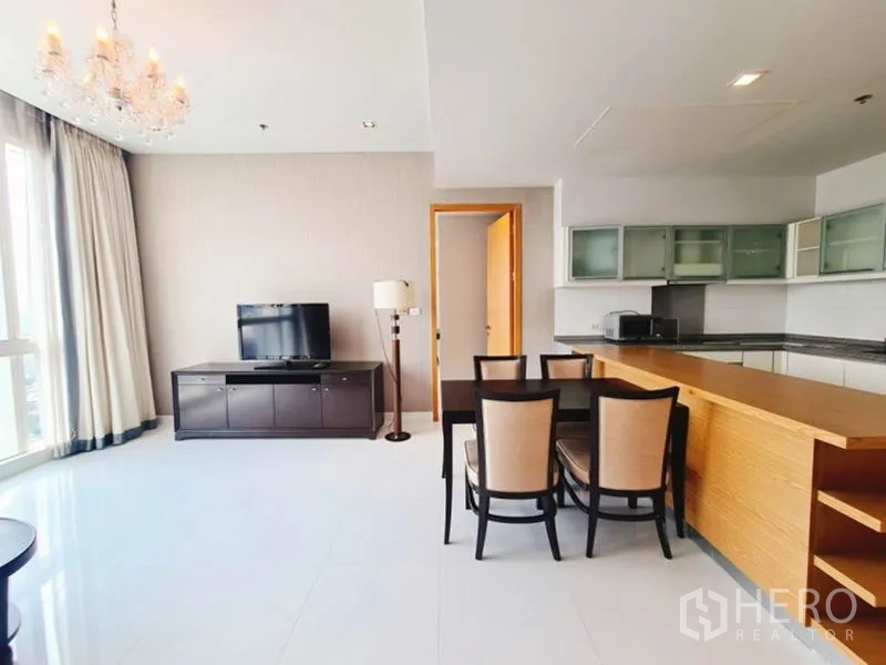 Condominium for rent in Khlong Toei, Bangkok - Dining area next to a long kitchen island, TV unit and tall curtains.