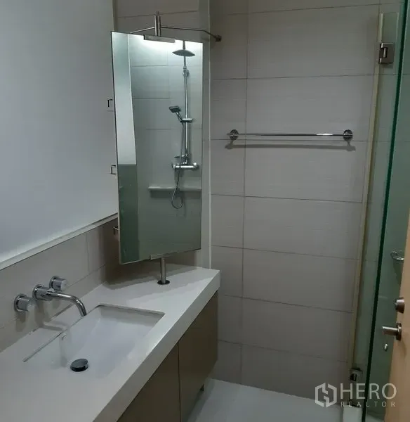 Condominium for rent in Khlong Toei, Bangkok - Contemporary bathroom featuring a vanity sink, mirror and a walk‑in rain shower with glass partition.