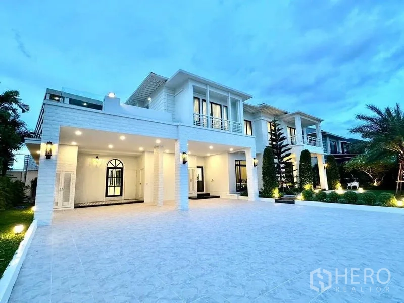 独立式住宅 出租在Bang Phli, Samut Prakan - 白色两层独栋别墅黄昏外观，宽阔铺砖车道与修剪整齐的花园。