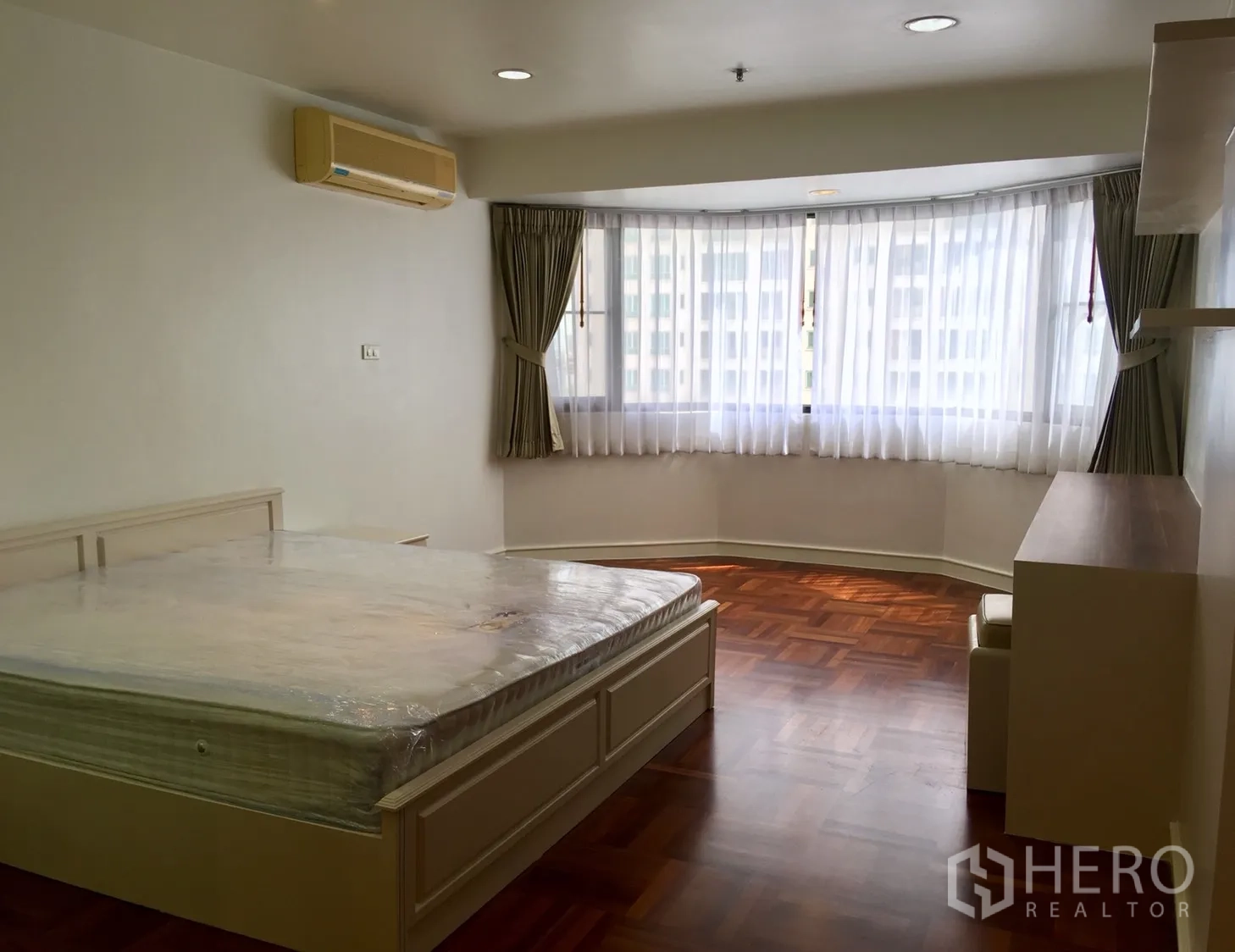 Condominium for rent or sale in Watthana, Bangkok - Spacious bedroom with bay window, sheer curtains and polished wood floors.