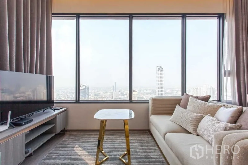 คอนโด ให้เช่าในWatthana, Bangkok - โซฟาและทีวีข้างหน้าต่างเต็มผนัง โต๊ะกลางหินอ่อนขนาดเล็ก พร้อมวิวเมืองแบบพาโนรามา