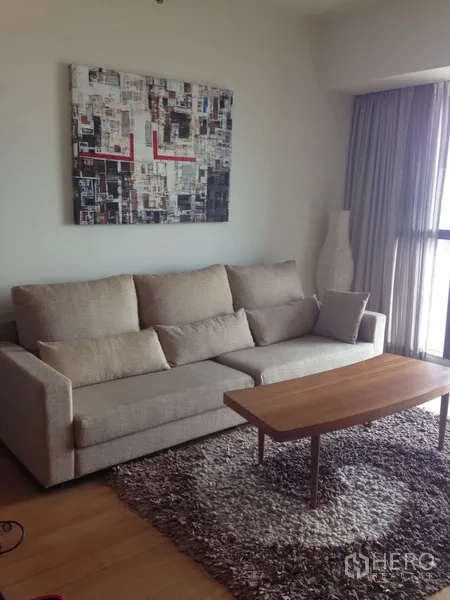 Condominium for rent in Sathon, Bangkok - Cozy lounge corner with beige sofa, shag rug, wooden coffee table, and wall art beside a full-height window.