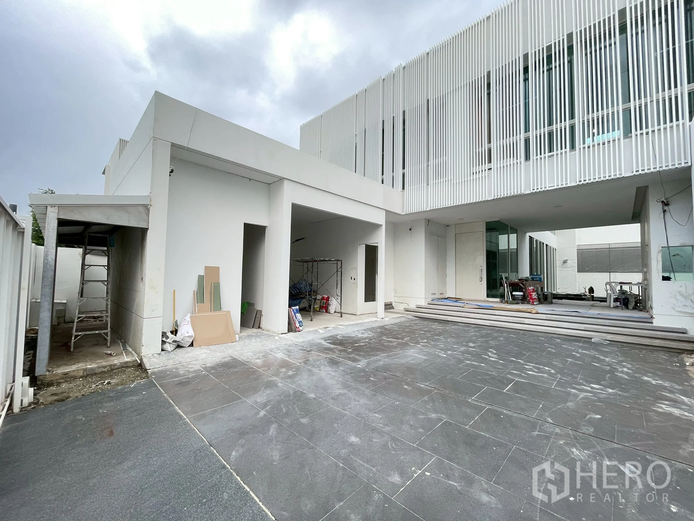 Detached House for sale in Bang Phli, Samut Prakan - Large tiled driveway and covered carport beside a white modern house under construction.