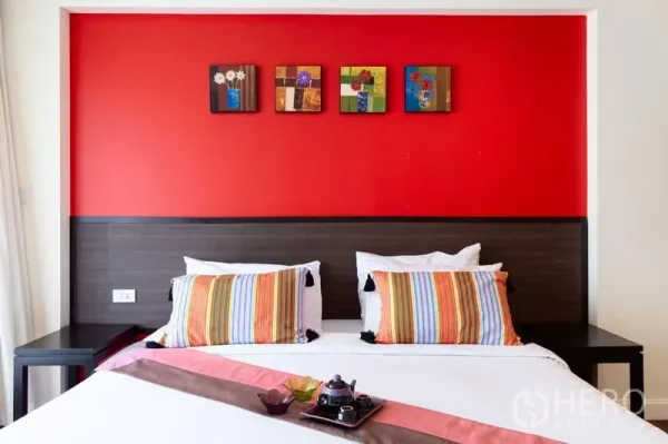 Condominium for rent in Bang Rak, Bangkok - Close-up of a king bed with striped pillows beneath a red feature wall and framed artwork.