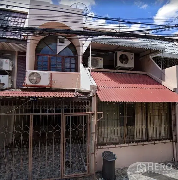 Townhouse for rent in Khlong Toei, Bangkok - Two-storey townhouse facade with gated entrance, metal awnings and exterior air-conditioning units.