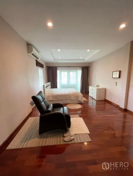 Detached House for rent - Generous primary bedroom with wood flooring, bed and lounge chair, recessed ceiling, and large windows.