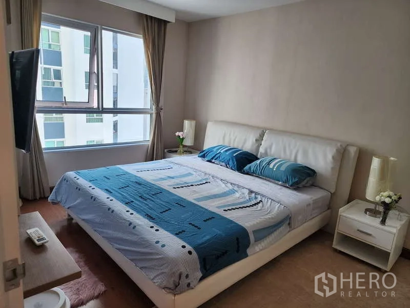 คอนโด ให้เช่าในHuai Khwang, Bangkok - ห้องนอนหลักเตียงขนาดใหญ่ โต๊ะข้างเตียง และหน้าต่างบานกว้างมองเห็นอาคารข้างเคียง