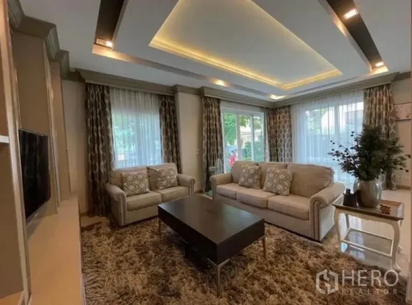 Detached House for rent or sale in Bang Phli, Samut Prakan - Bright living room with coffered ceiling lighting, two sofas, large windows and a plush rug.