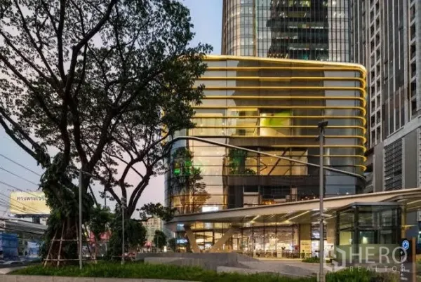 คอนโด ให้เช่าในHuai Khwang, Bangkok - อาคารผสมผสานสมัยใหม่ ฟาซาดโค้งเส้นสีทองและร้านค้าชั้นล่างยามค่ำ