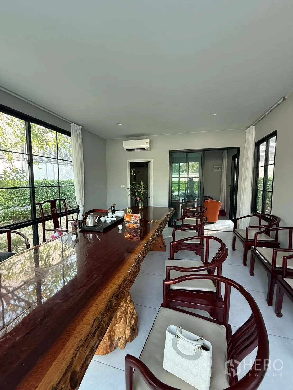 独栋房屋 for rent in Bang Kapi, Bangkok - 落地窗休闲室，整块原木长桌与古典椅，面向花园景观。
