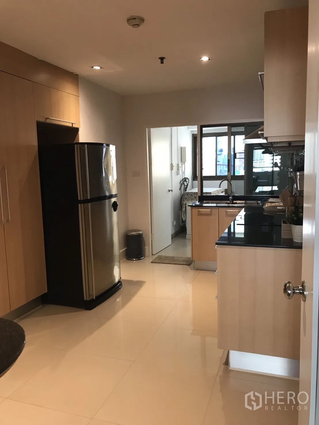 Condominium for rent in Bangkok - Kitchen view with stainless refrigerator leading toward a utility and laundry area.