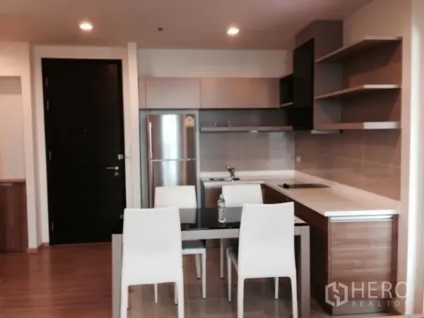 Condominium for rent in Khlong Toei, Bangkok - Modern open kitchen with built-in cabinets, electric cooktop, refrigerator, and a four-seat dining table.