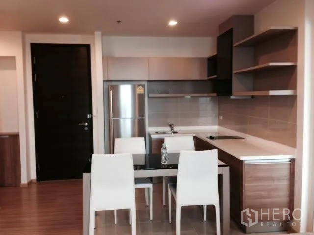 Condominium for rent in Khlong Toei, Bangkok - Modern open kitchen with built-in cabinets, electric cooktop, refrigerator, and a four-seat dining table.