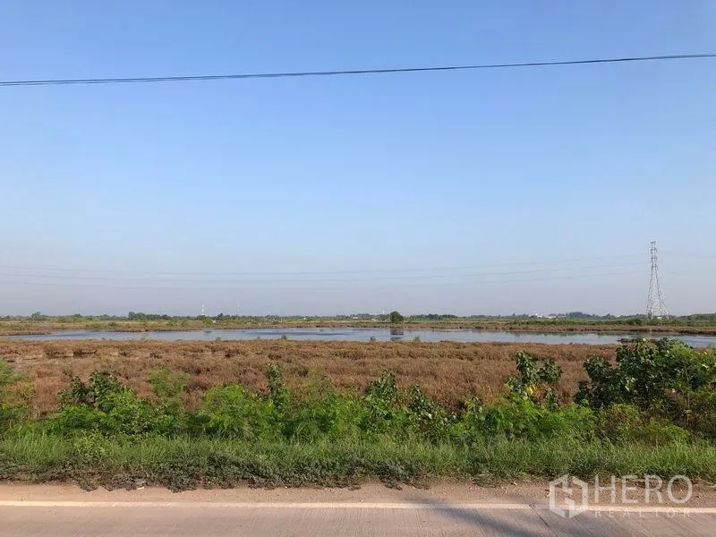 Land for sale in Mueang Samut Sakhon, Samut Sakhon - Roadside view across the plot toward ponds and a transmission tower in the distance.