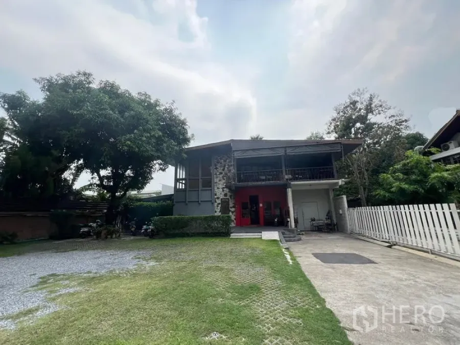 Detached House for rent in Khlong Toei, Bangkok - Front yard view with wide grass lawn, gravel parking and white picket fence of the detached home.