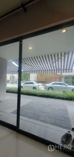 带办公室的家 出租在Prawet, Bangkok - 一层落地玻璃门外的条纹遮阳篷与街边停车位。