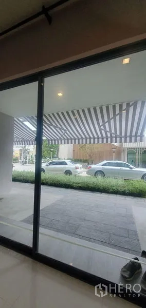带办公室的家 出租在Prawet, Bangkok - 一层落地玻璃门外的条纹遮阳篷与街边停车位。