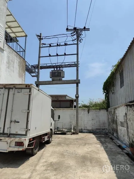 Factory for sale in Sai Noi, Nonthaburi - Truck parking and loading yard with transformer structure at the factory.