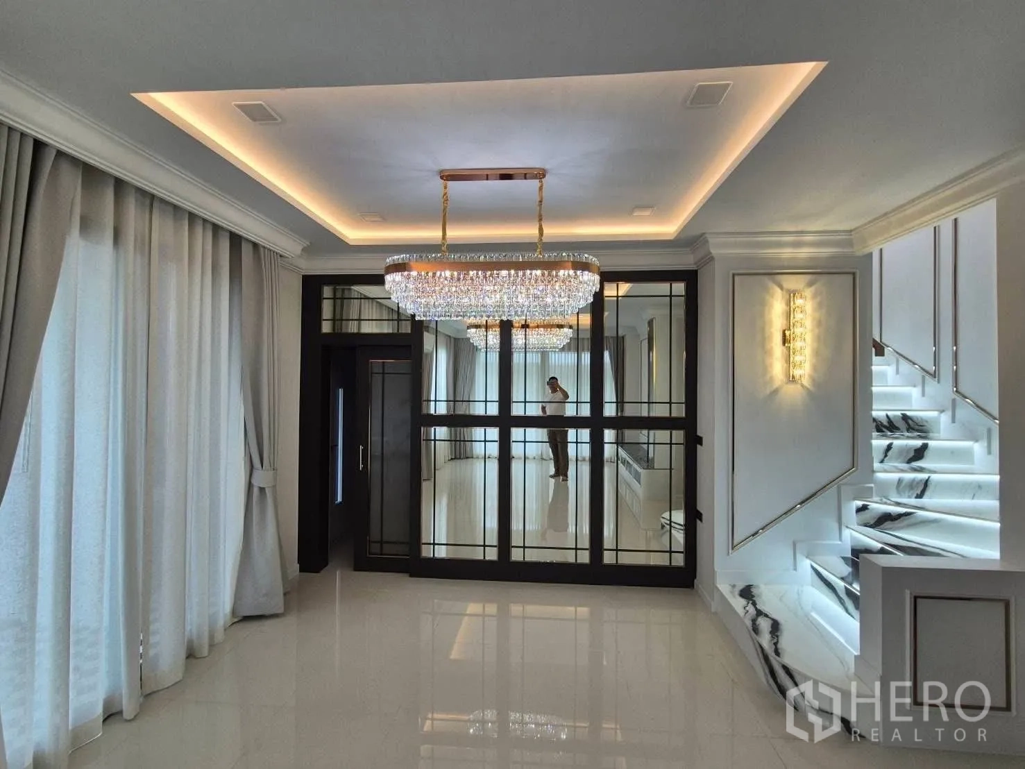 Detached House for sale in Bang Kruai, Nonthaburi - Living area view with glass partition, ceiling lights and illuminated marble staircase.
