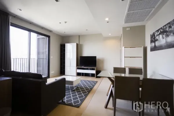 公寓 出租在Watthana, Bangkok - 宽敞起居区，电视柜、玻璃门通向阳台及用餐角，配色简洁。